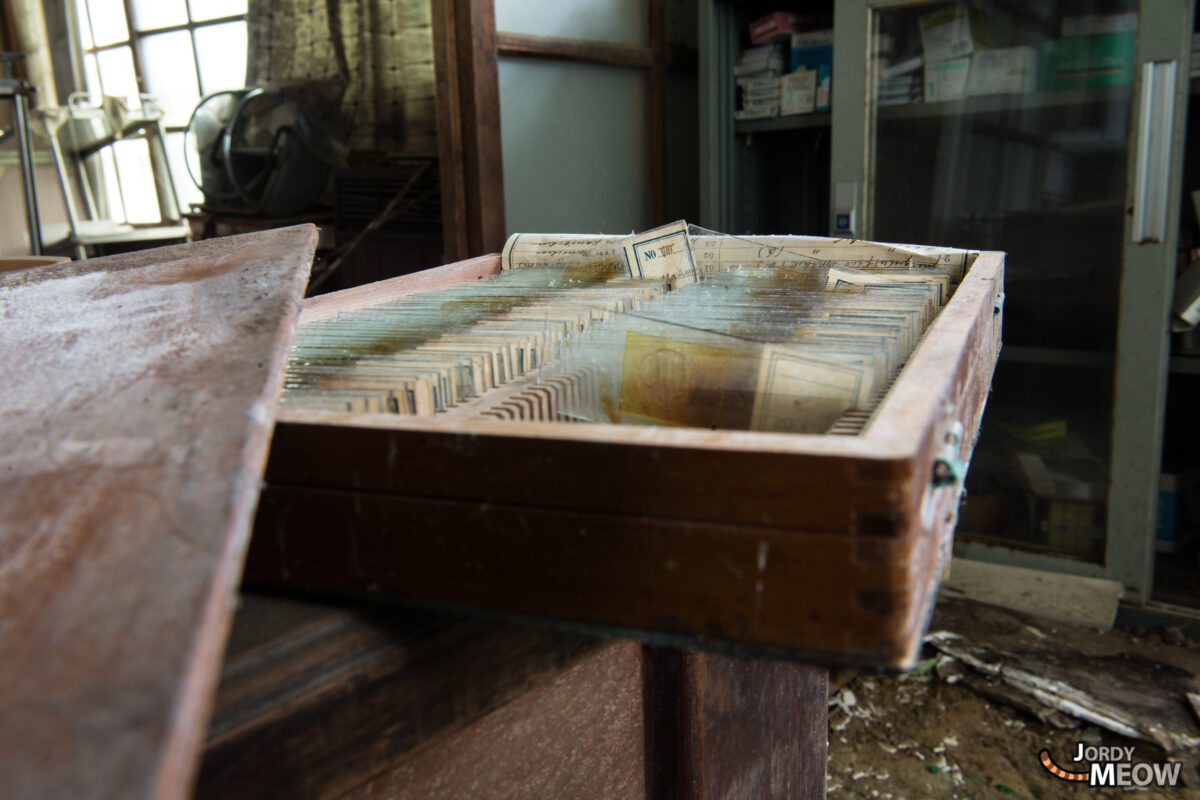 Open drawer of patient records in abandoned clinic office, dusty desk and cabinets behind.