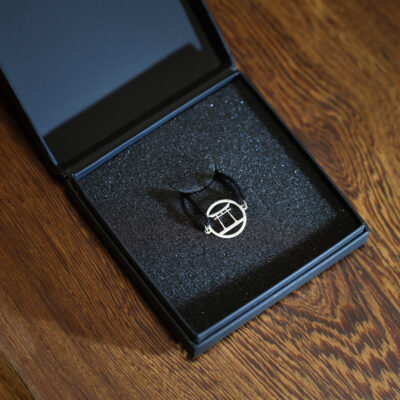 Silver geometric pendant necklace in open black foam gift box on wooden table.