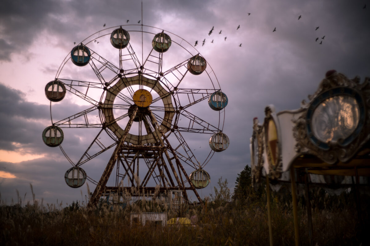 Abandoned Ferris wheel in overgrown amusement park at dusk under stormy sky