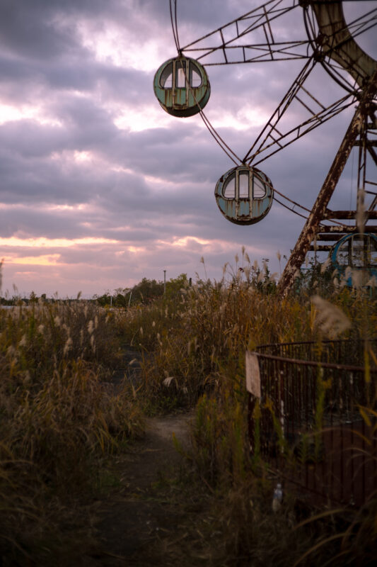 Abandoned Ferris wheel at Kejonuma Leisure Land amid overgrown weeds at dusk