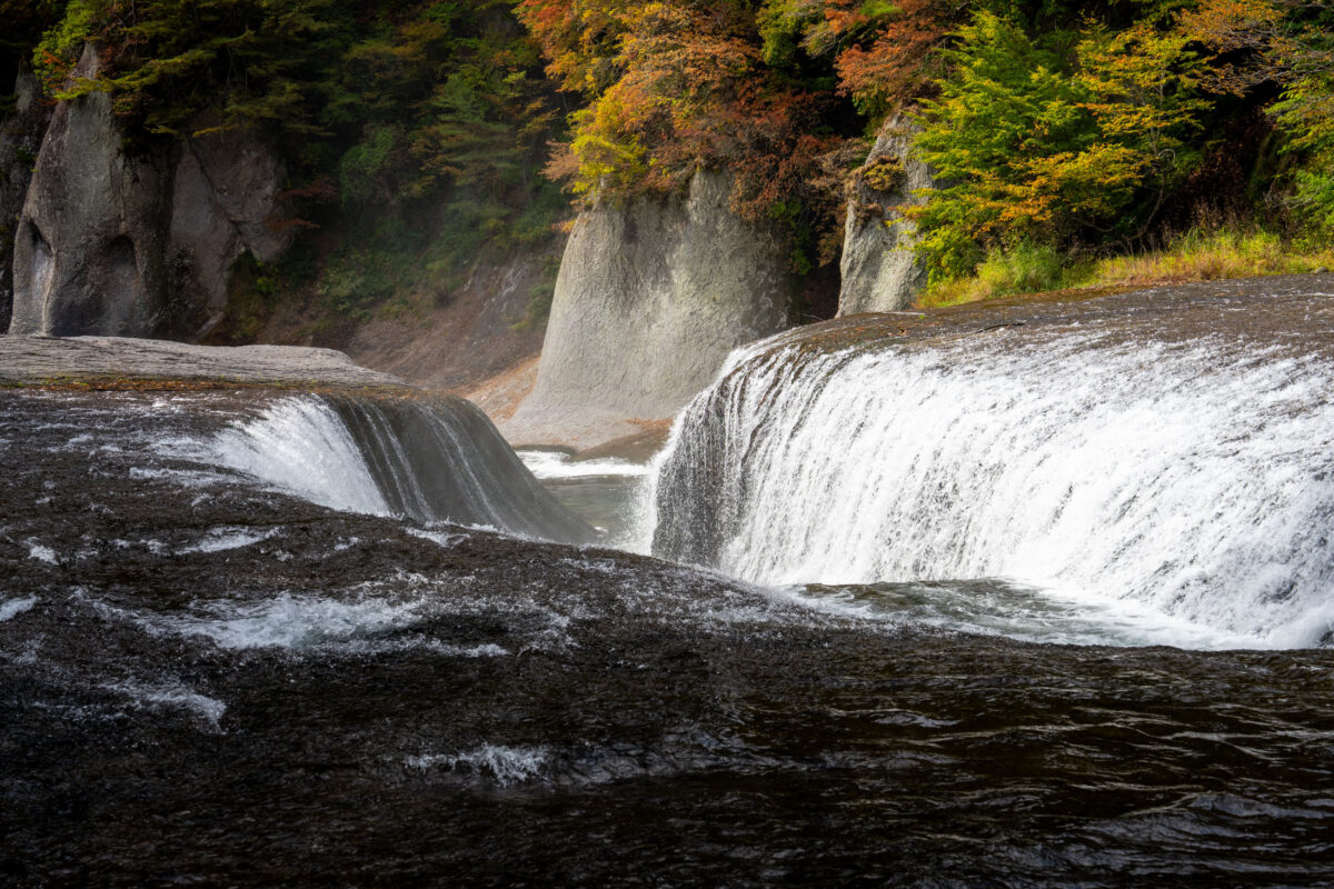 Fukiware Falls wide waterfall cascading over dark rocks in autumn gorge, Japan