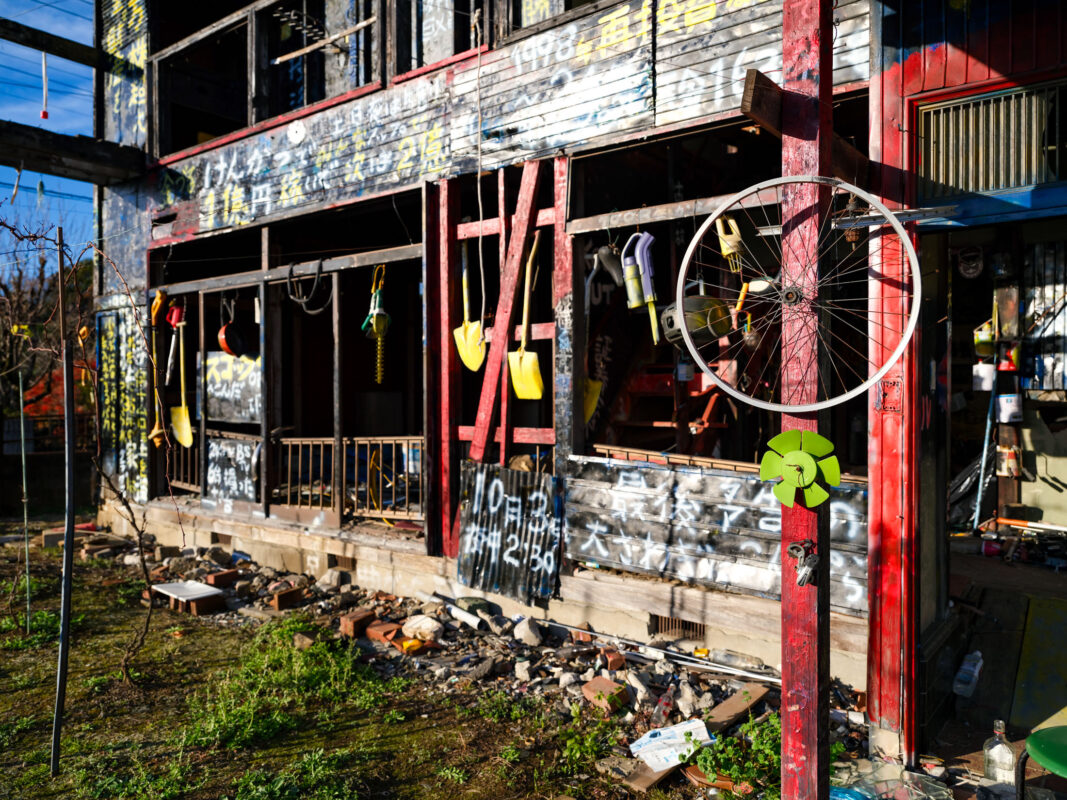 Sunlit graffiti-covered abandoned wooden house with hanging tools, ladders, and bicycle wheel