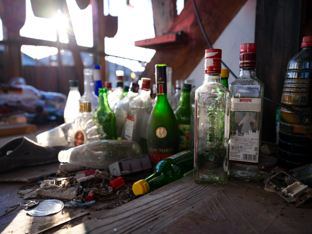 Sunlit abandoned house floor littered with empty liquor bottles and broken glass