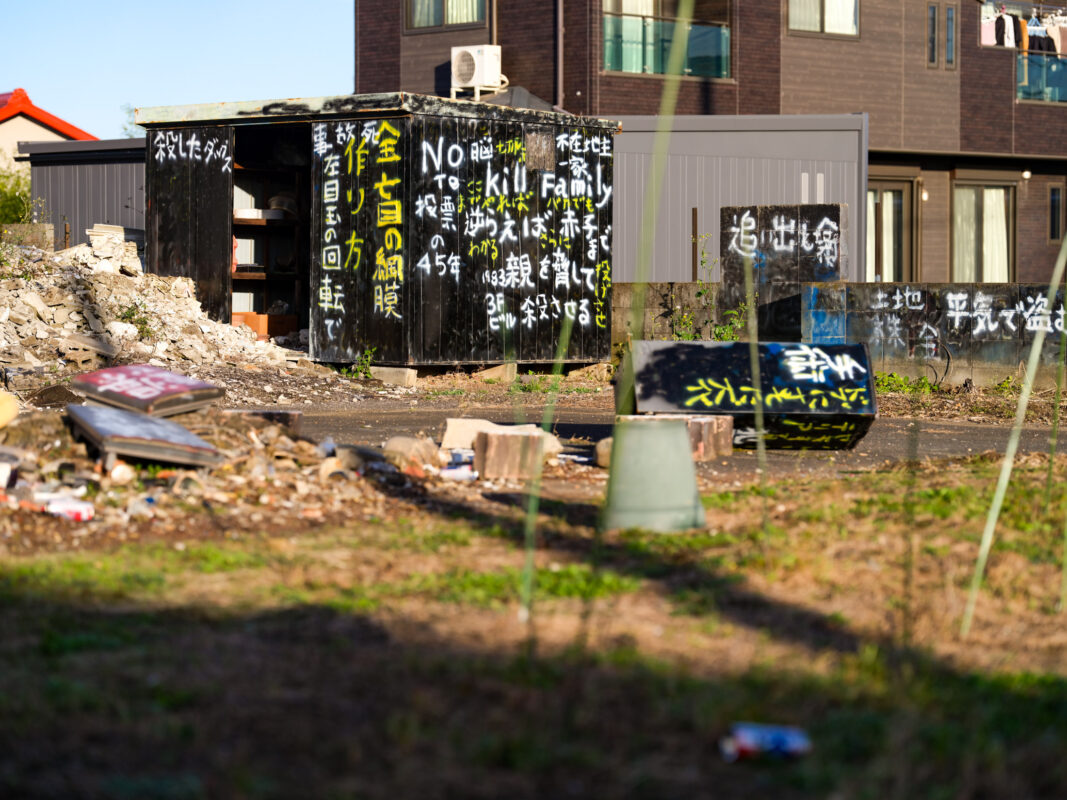 Graffiti-covered black protest shack on debris lot, contrasting with modern apartments behind
