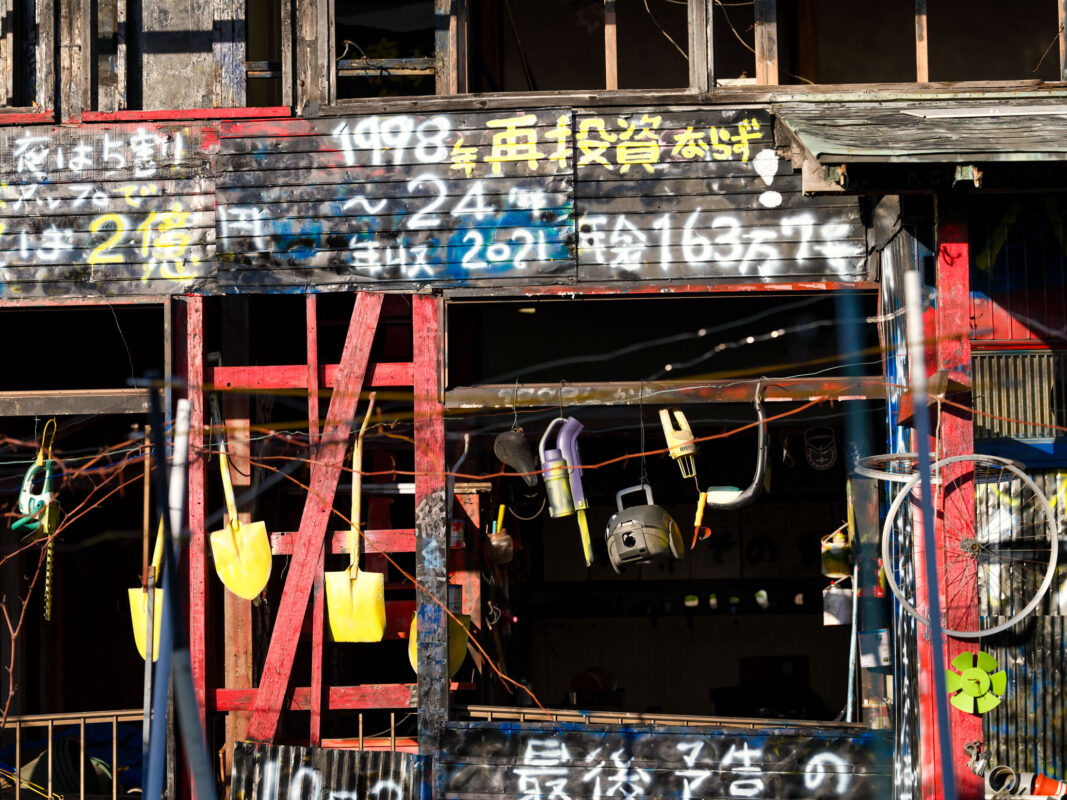 Charred abandoned wooden house covered in Japanese graffiti, exposed beams, and missing walls.
