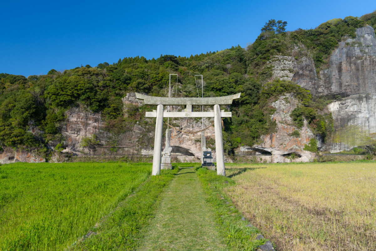 Stone torii gate on farm path with Yabakei cliffs, rural Japan landscape.