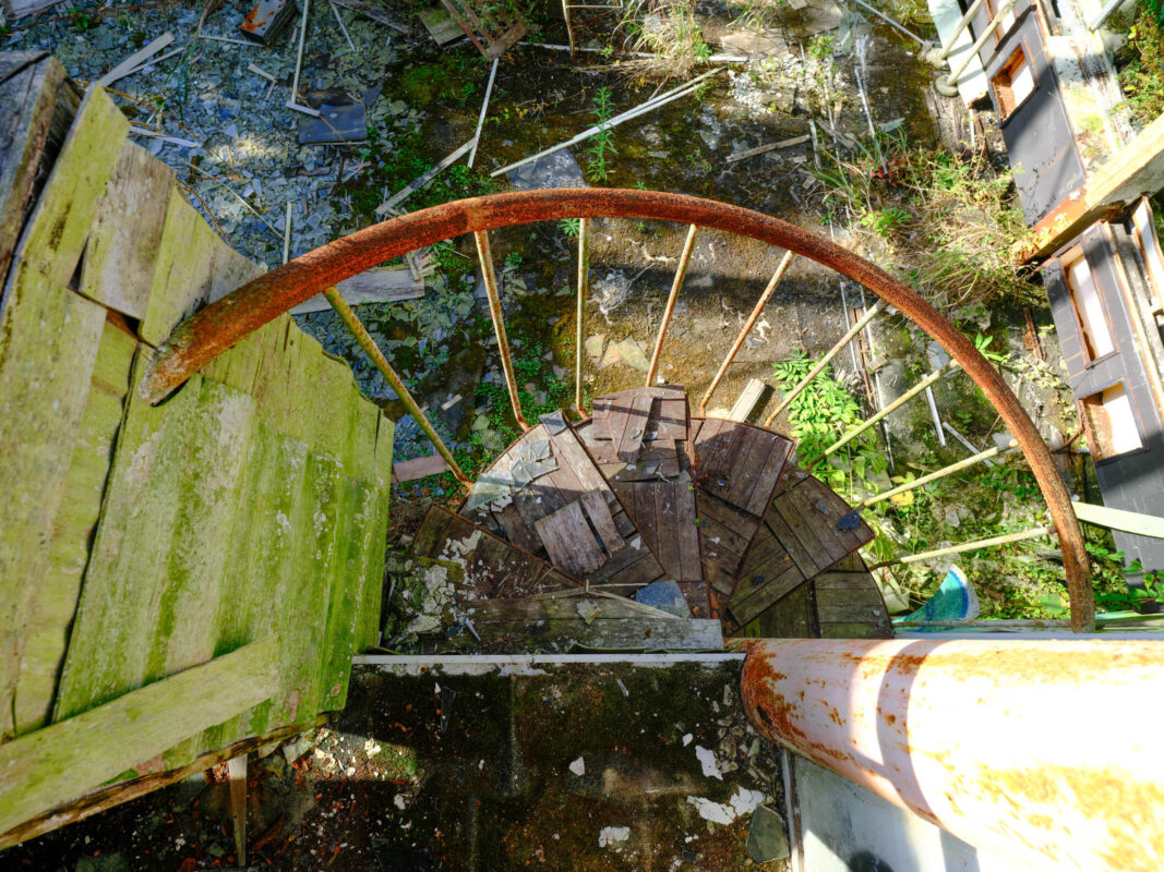 Top-down view of broken spiral staircase in abandoned church, rusted railing and mossy debris