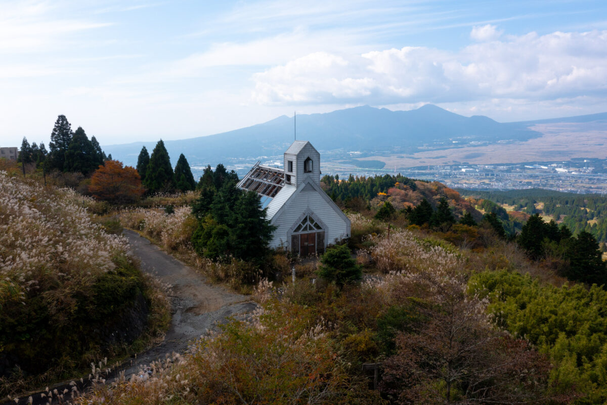 Abandoned white hillside church with damaged roof overlooking valley and distant mountains