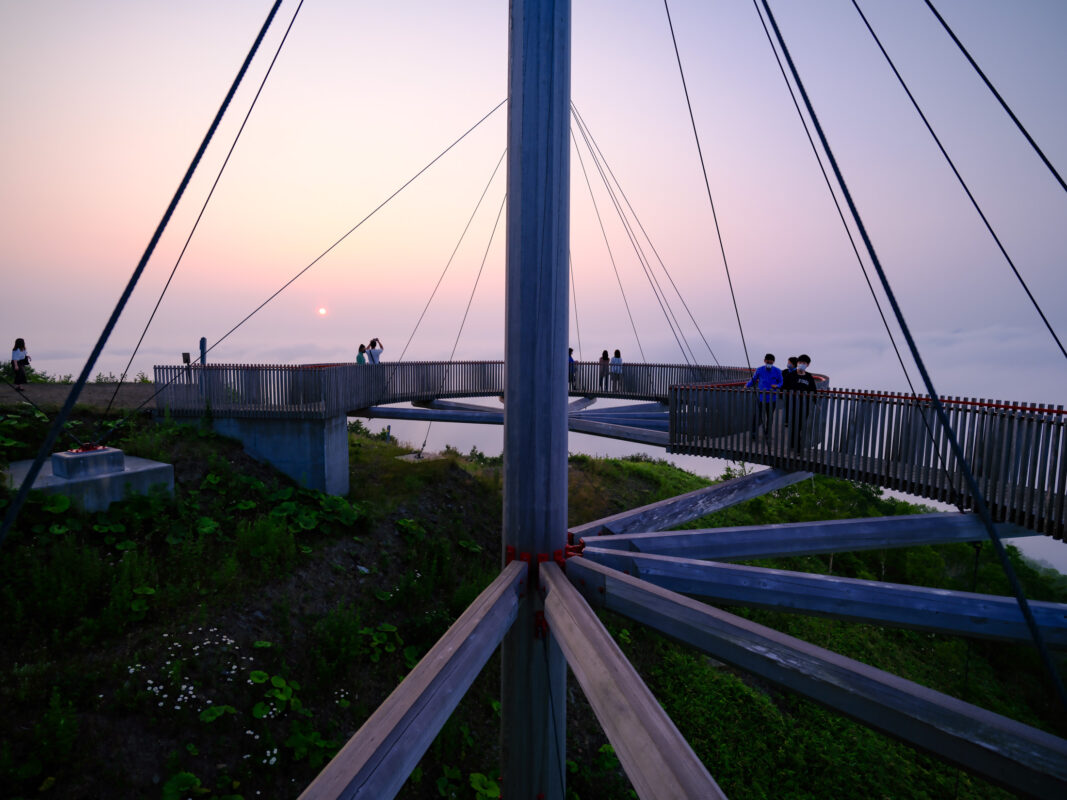 Unkai Terrace skywalk at dusk, cable-supported walkway above forested mountains with visitors