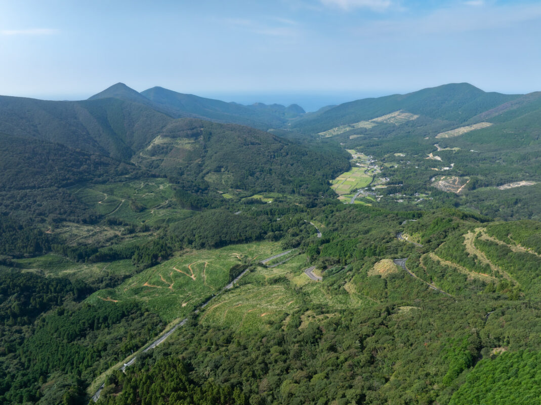 Aerial view of Ayumodoshi Natural Park green mountains, forested valley, and winding road