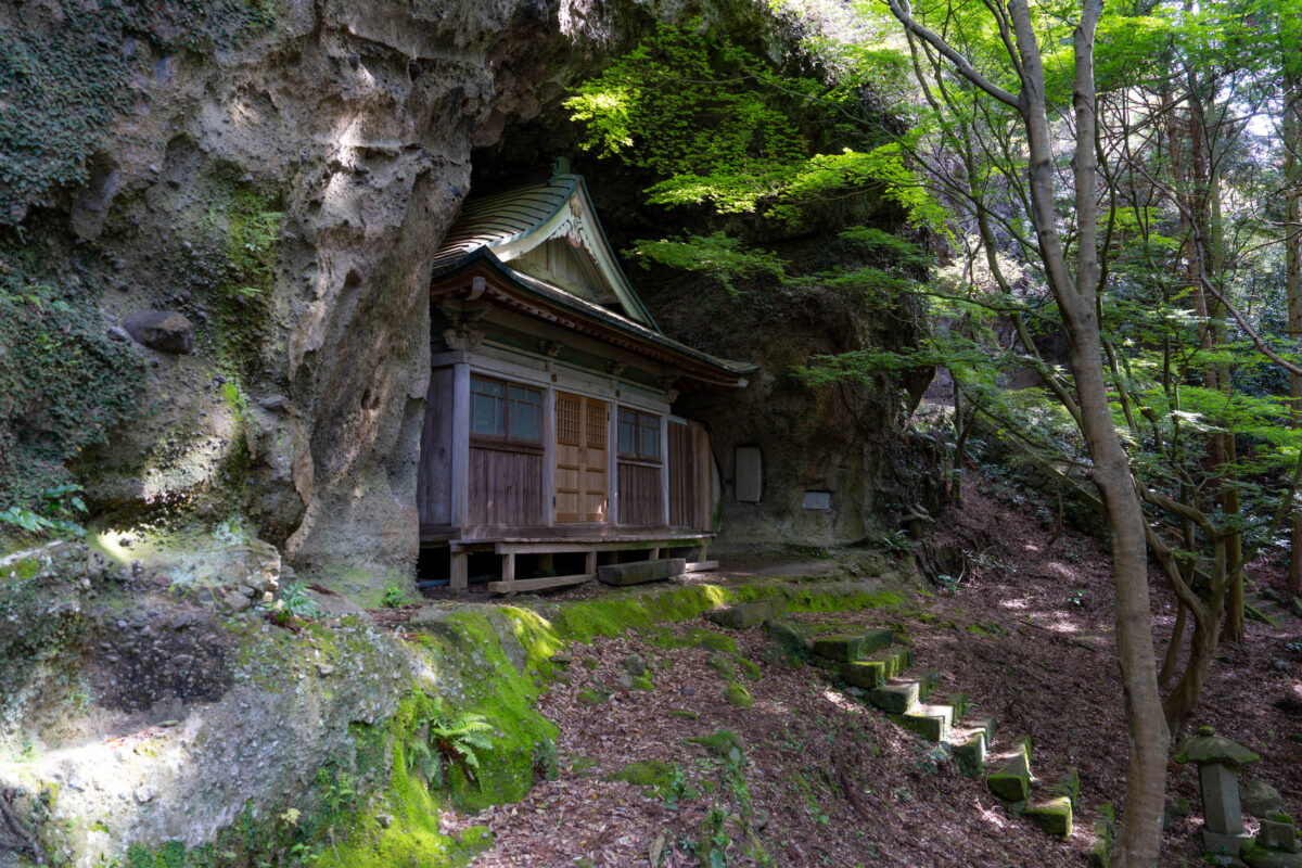Hidden Kyu-Sento-ji cliffside temple, wooden hall under rock overhang in lush forest.