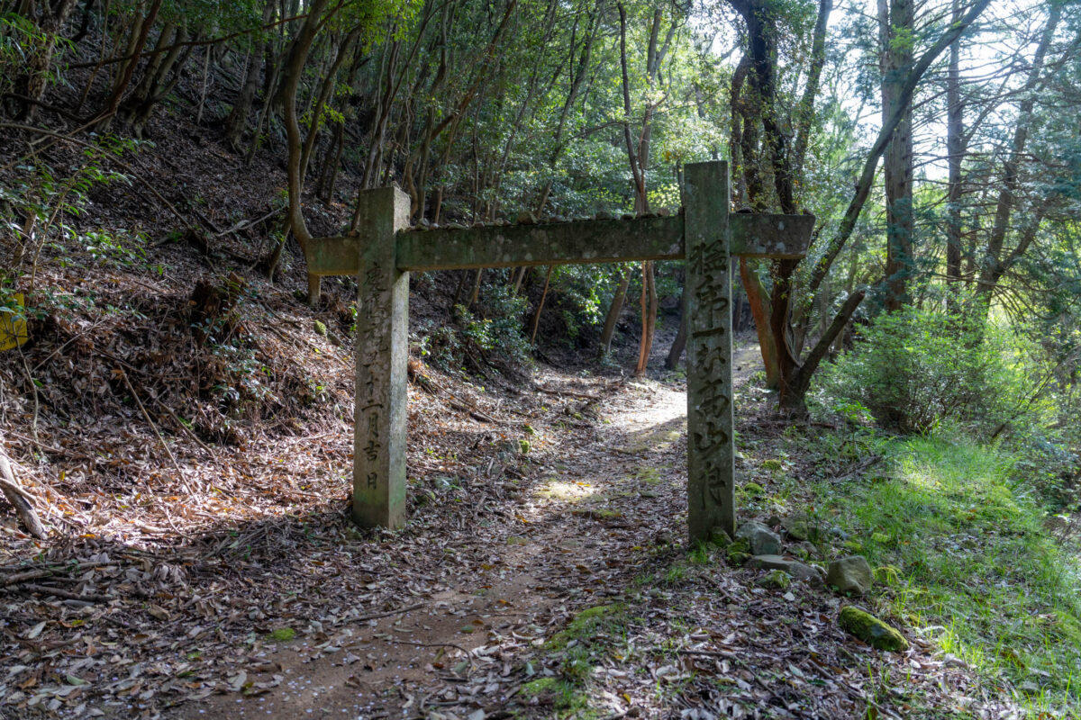 Weathered wooden torii gate on leaf-covered forest path to Kyu-Sento-ji temple site