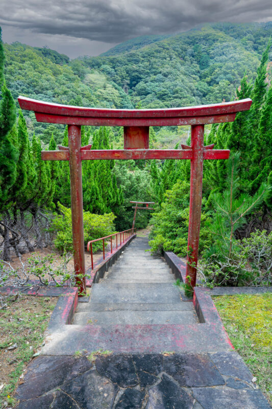 Weathered red torii gate over mossy stone steps on misty forest shrine path