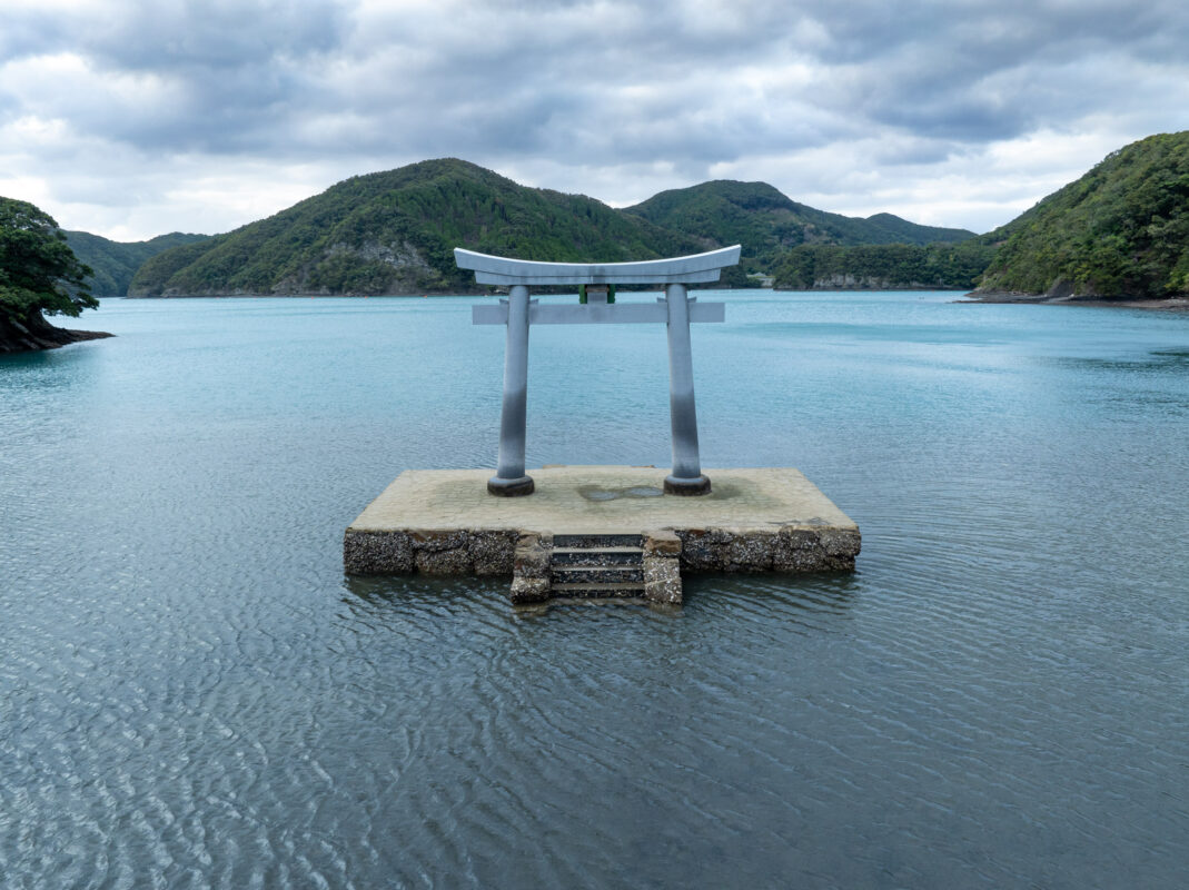 Watazumi Shrine torii gate standing in shallow sea water with forested hills in Japan