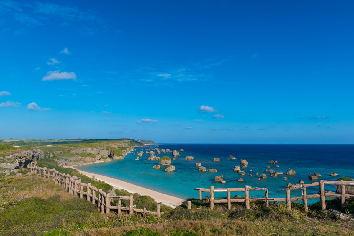 Elevated view of Miyako Island beach with turquoise water, rocky islets, and wooden fence.