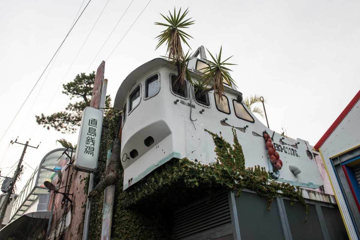 Naoshima Japan street with ship-like building, palm trees, vines, and Japanese sign