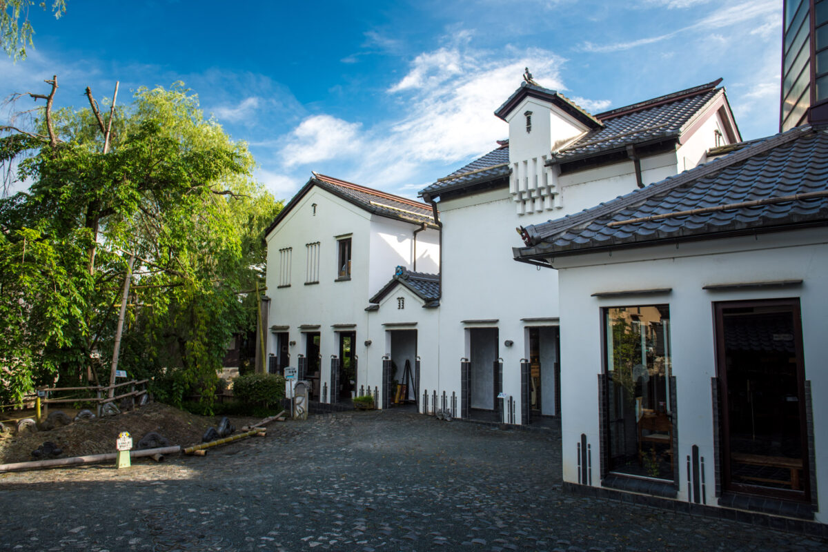 White-walled traditional buildings and cobblestone courtyard in Omihachiman, Japan under blue sky.