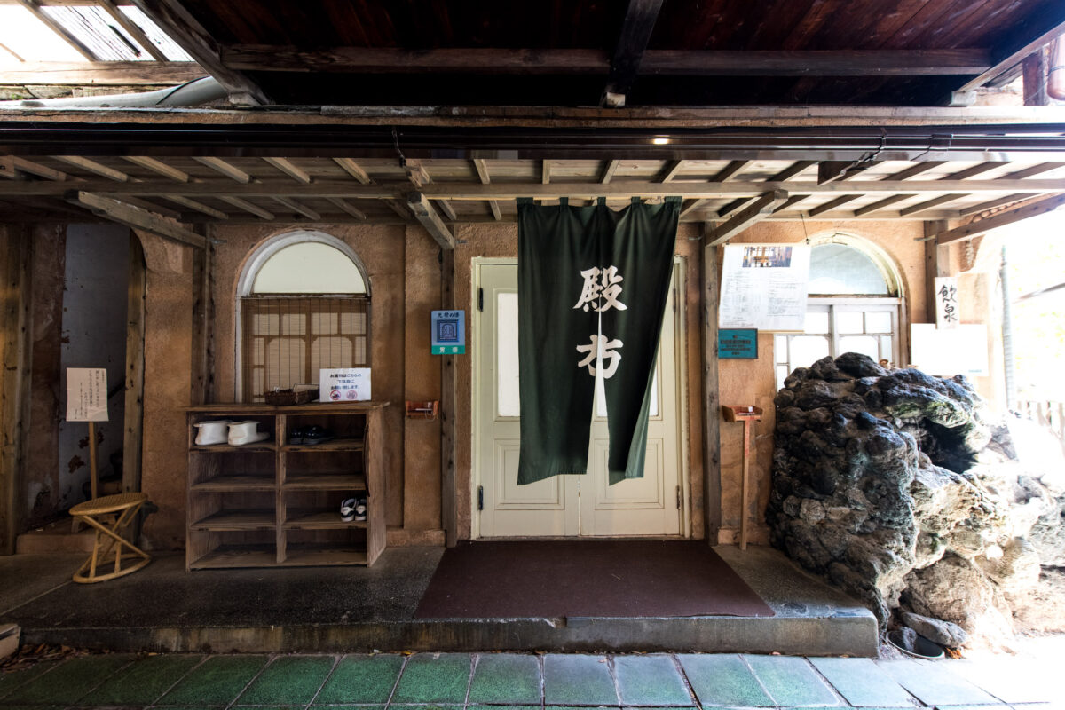 Entrance of Sekizenkan Ryokan, traditional Japanese inn with green noren curtain and stone wall.