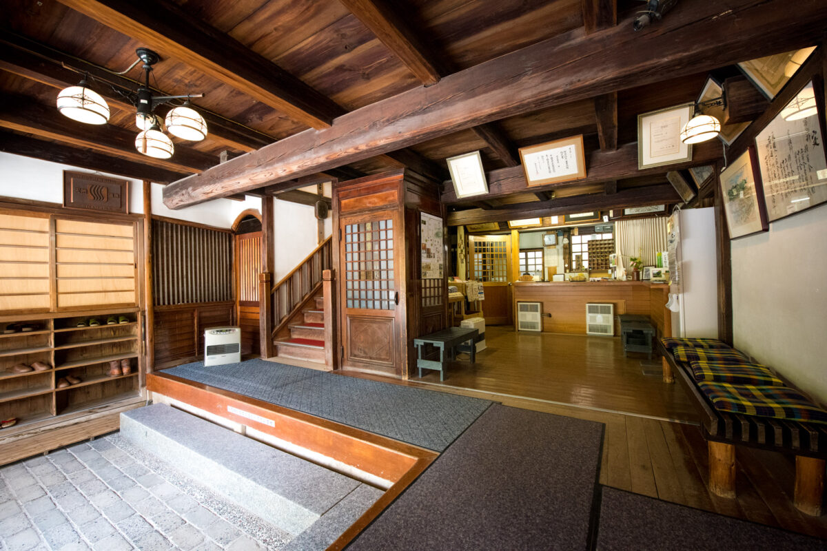 Sekizenkan Ryokan genkan entrance and reception with wooden floors, shoe shelves, warm lighting.