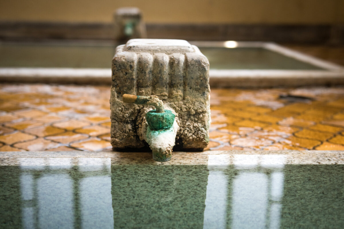 Weathered stone spout pours hot spring water into onsen pool at Sekizenkan Ryokan
