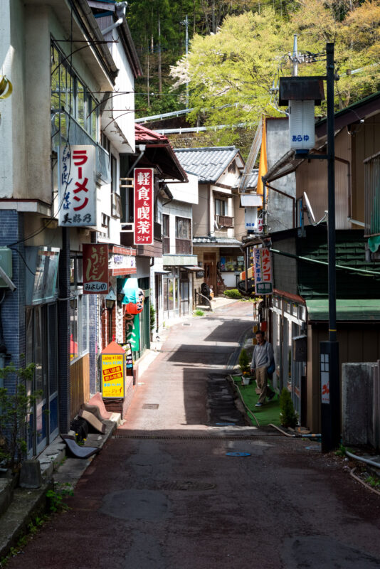 Narrow uphill alley in Sekizenkan Onsen town with traditional ryokan buildings and Japanese signs.