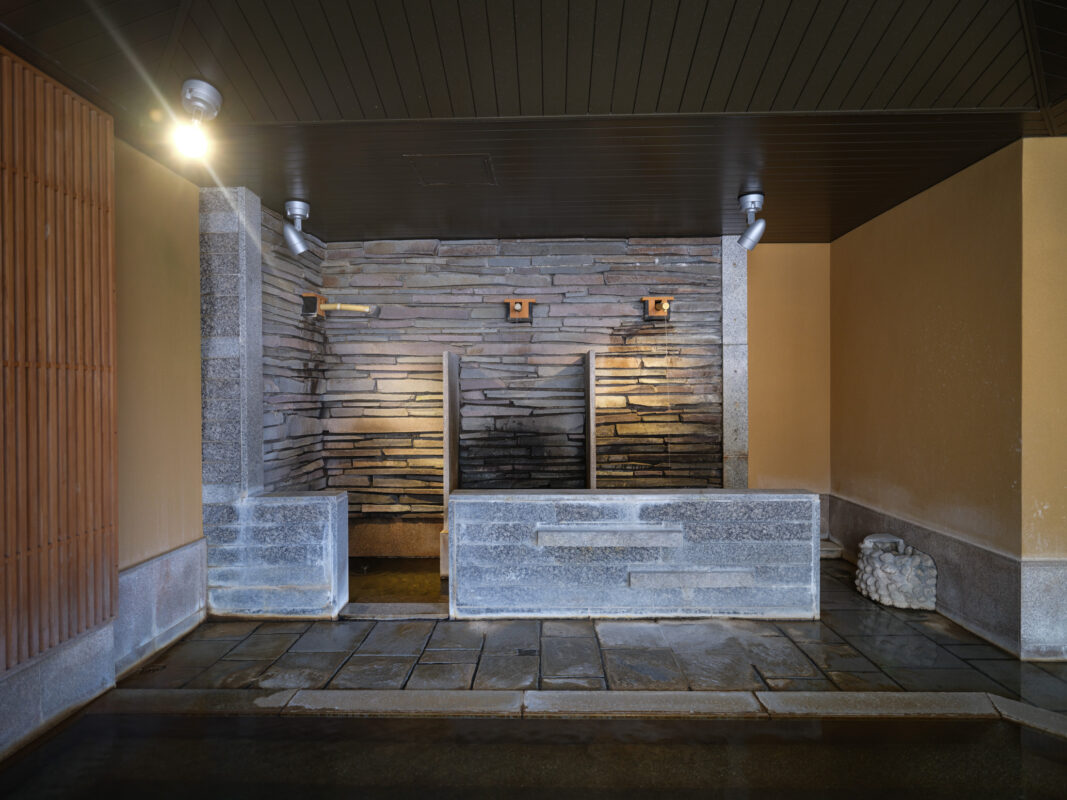 Symmetrical Shima Onsen hot spring stone basin with cascading water and warm recessed lighting.