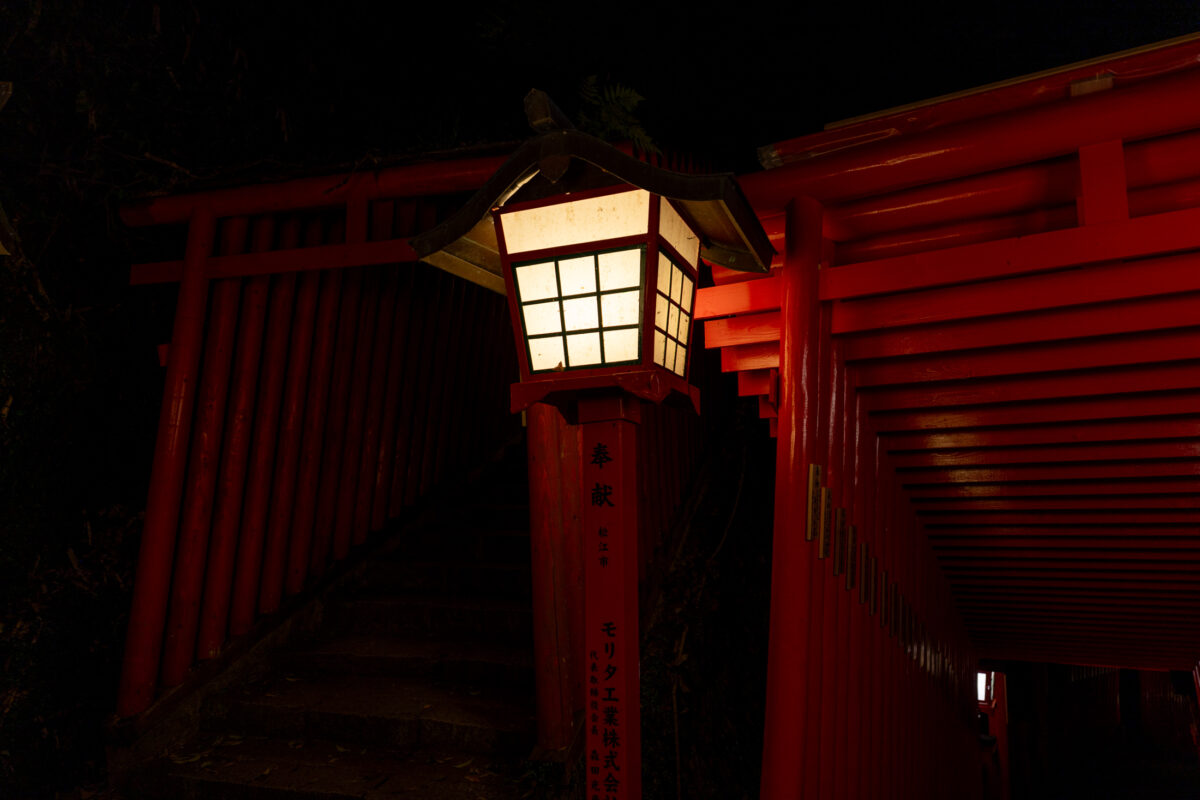 Lantern-lit vermilion torii gate tunnel at Taikodani Inari-jinja Shrine at night.
