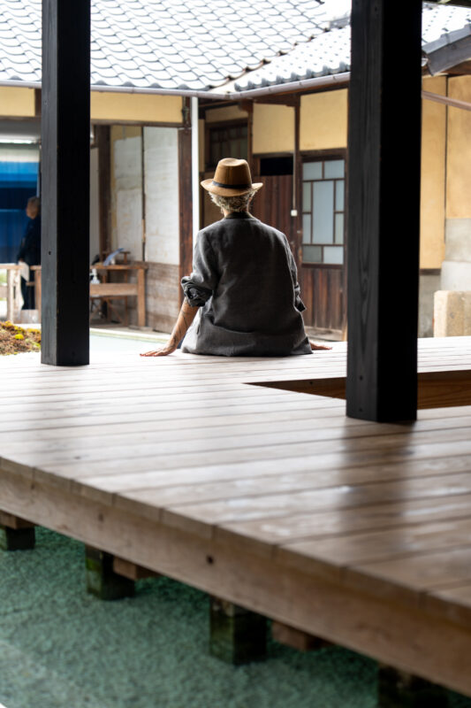 Person sitting on a traditional Japanese engawa in Naoshima, serene wooden corridor scene.