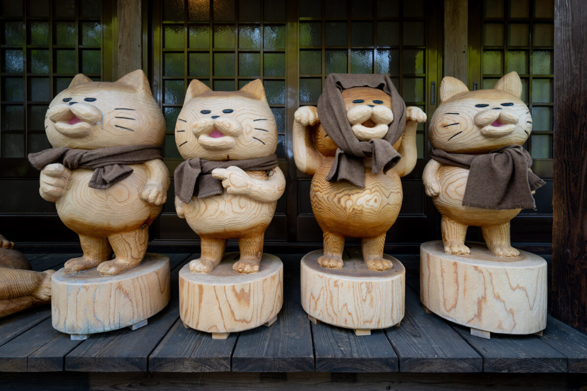 Four wooden cat statues with bibs lined up at Unrin-ji Temple, Japan