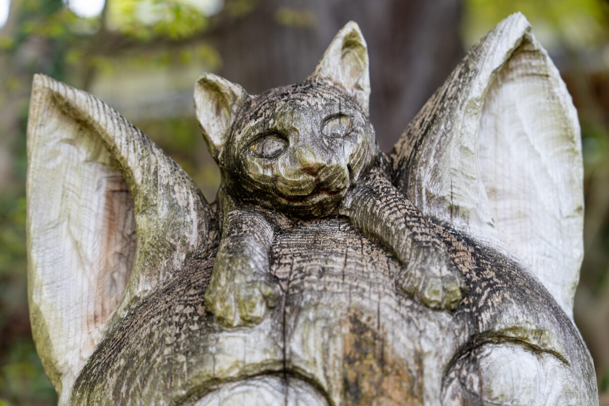 Weathered wooden cat sculpture at Unrin-ji Temple, Japan, in a leafy garden setting.
