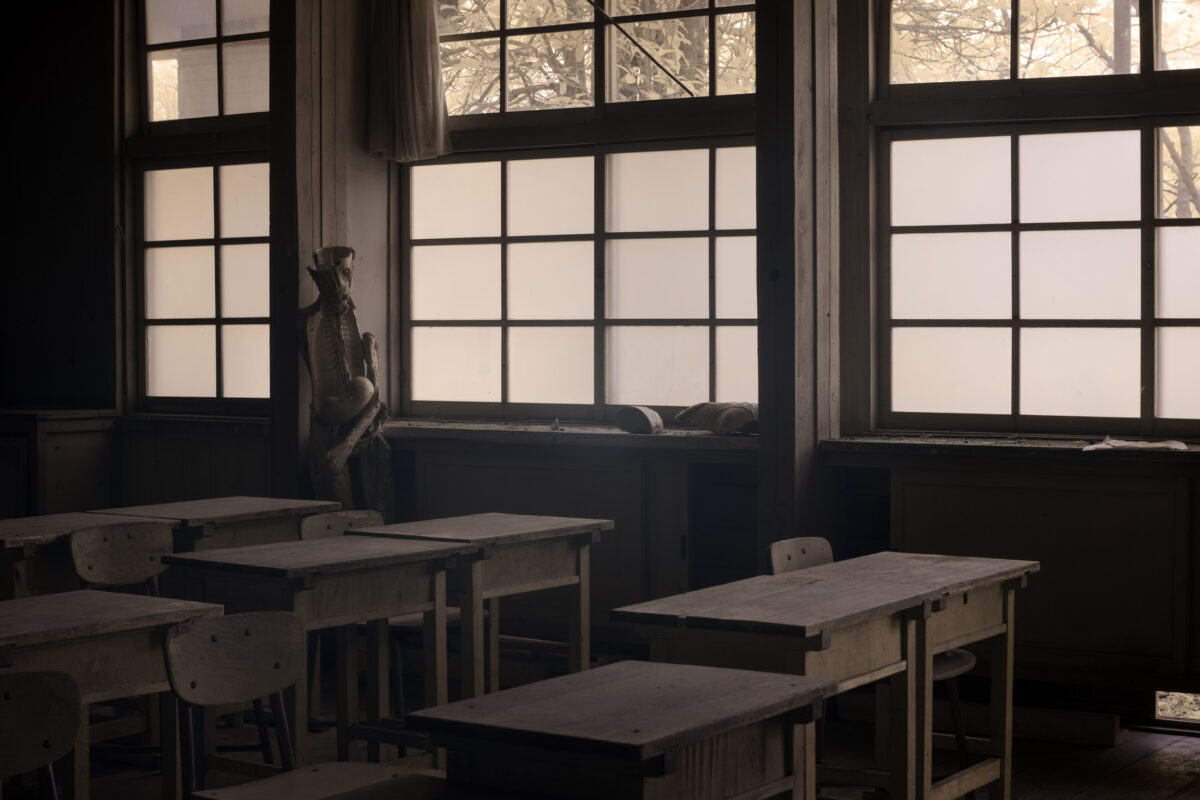 Foggy abandoned classroom with dusty desks and mannequin by window, Silent Hill atmosphere.