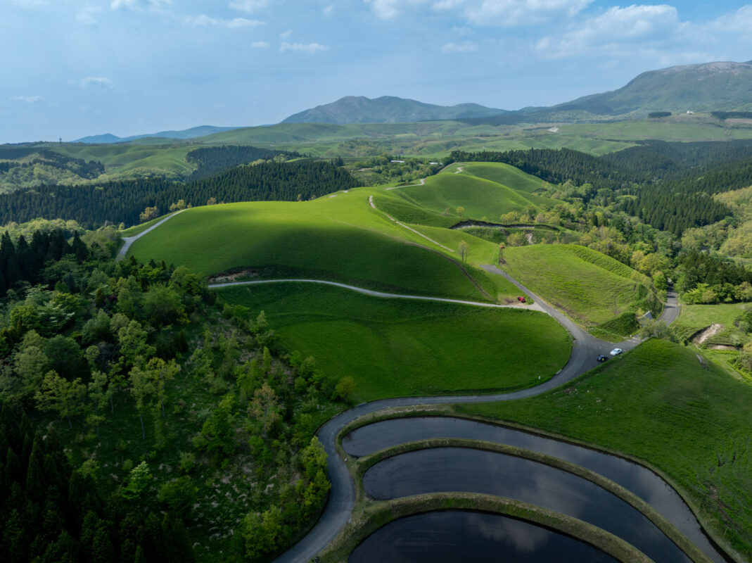 Aerial view of Japan’s Ogi rice terraces with reflective paddies, winding road, and distant mountains.