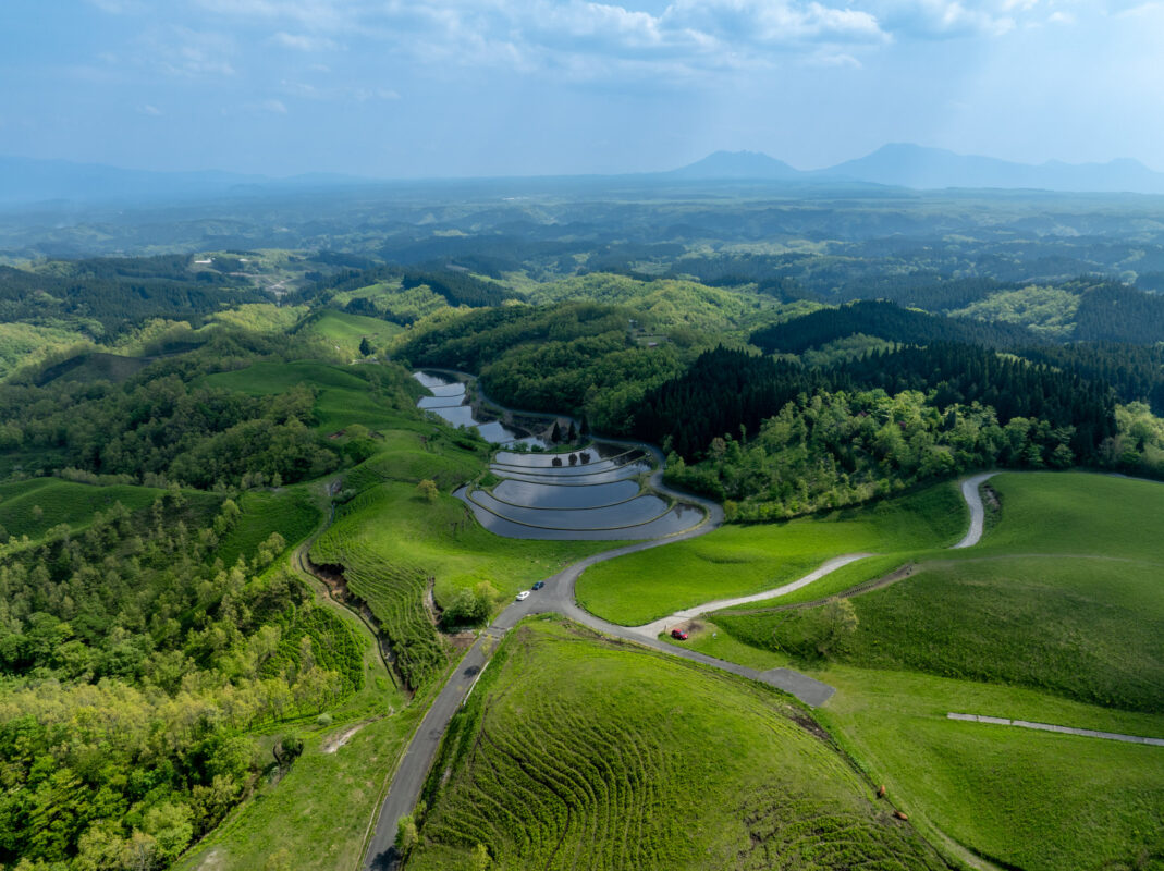 Aerial view of Ogi terraced rice fields, green hills, winding roads, and distant mountains.