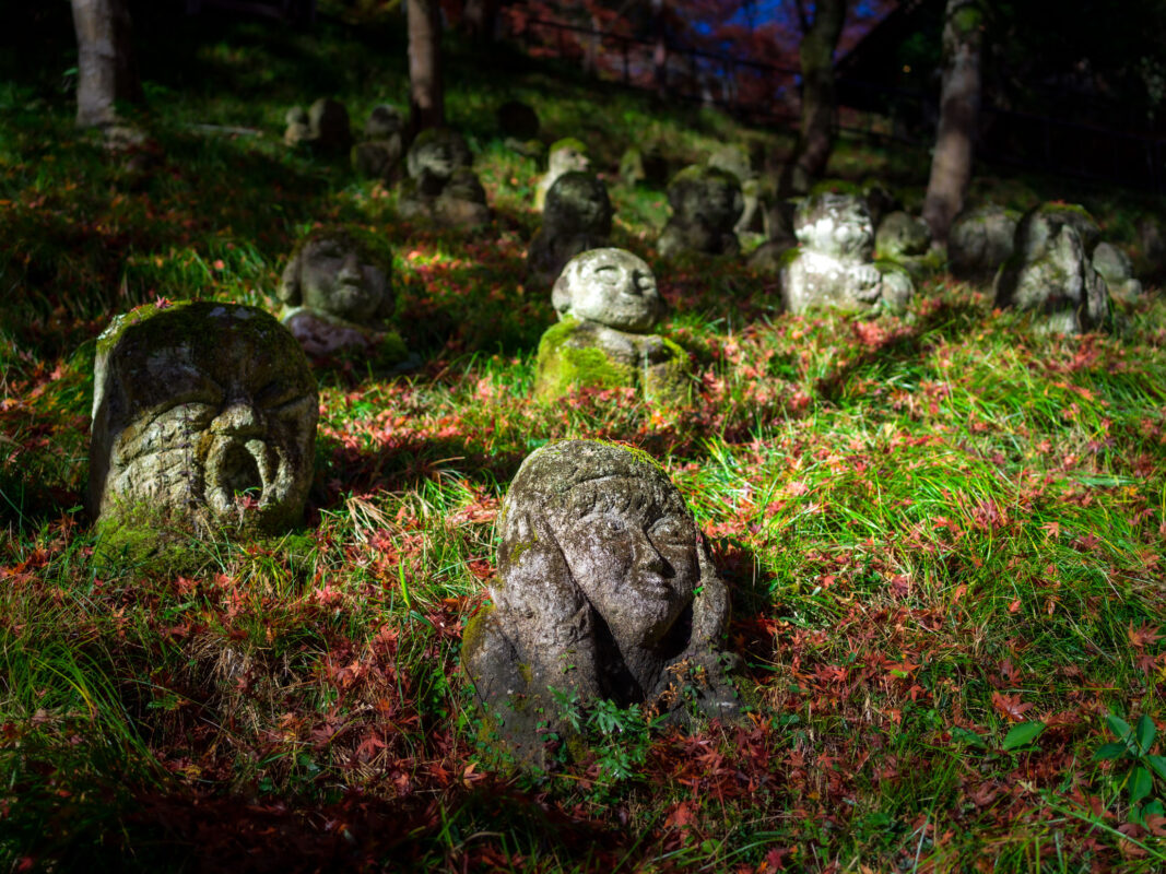 Moss-covered stone Buddha statues on an autumn hillside at Otagi Nenbutsu-ji Temple, Kyoto